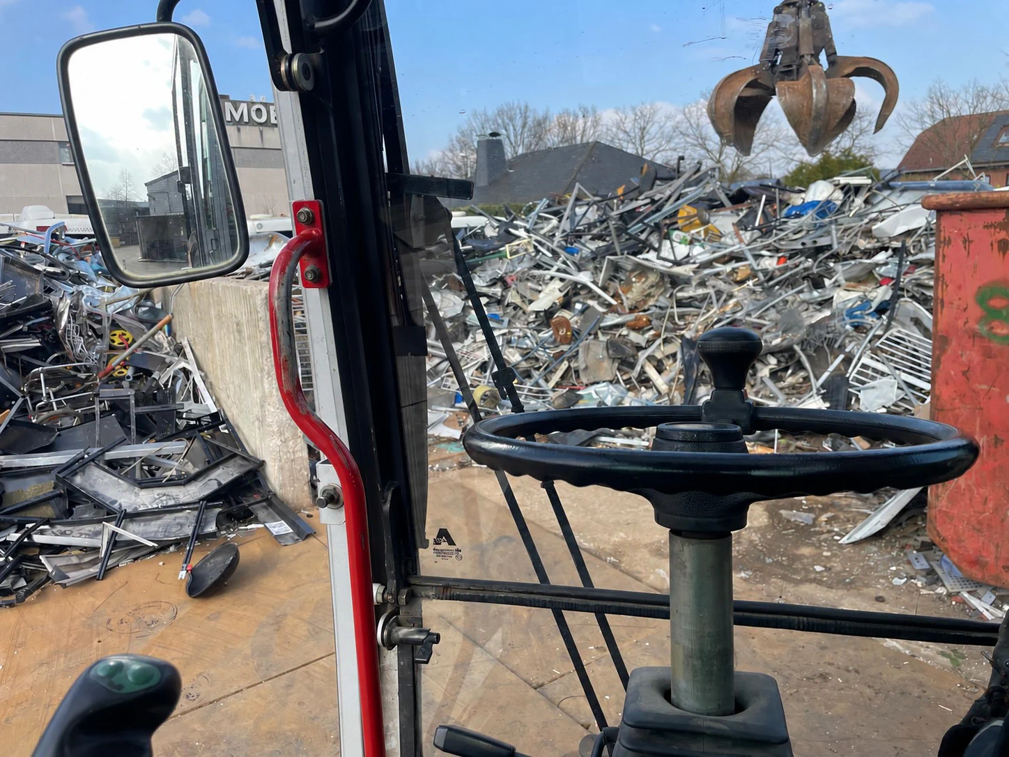 Blick aus der Baggerkabine auf den Schrottplatz mit Metallgreifer